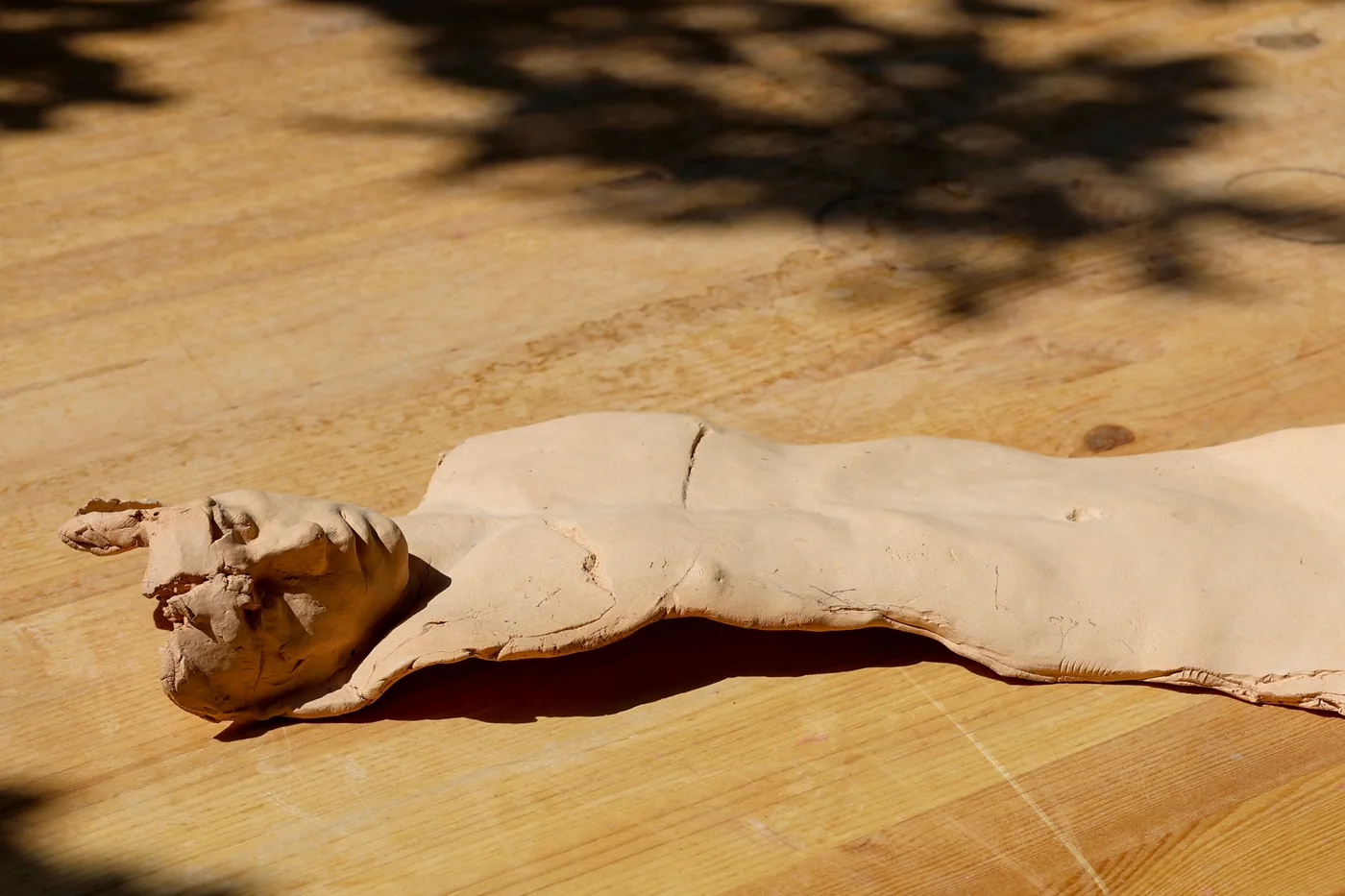a clay figure lying face up on a wooden table in sunlight, head turned to one side