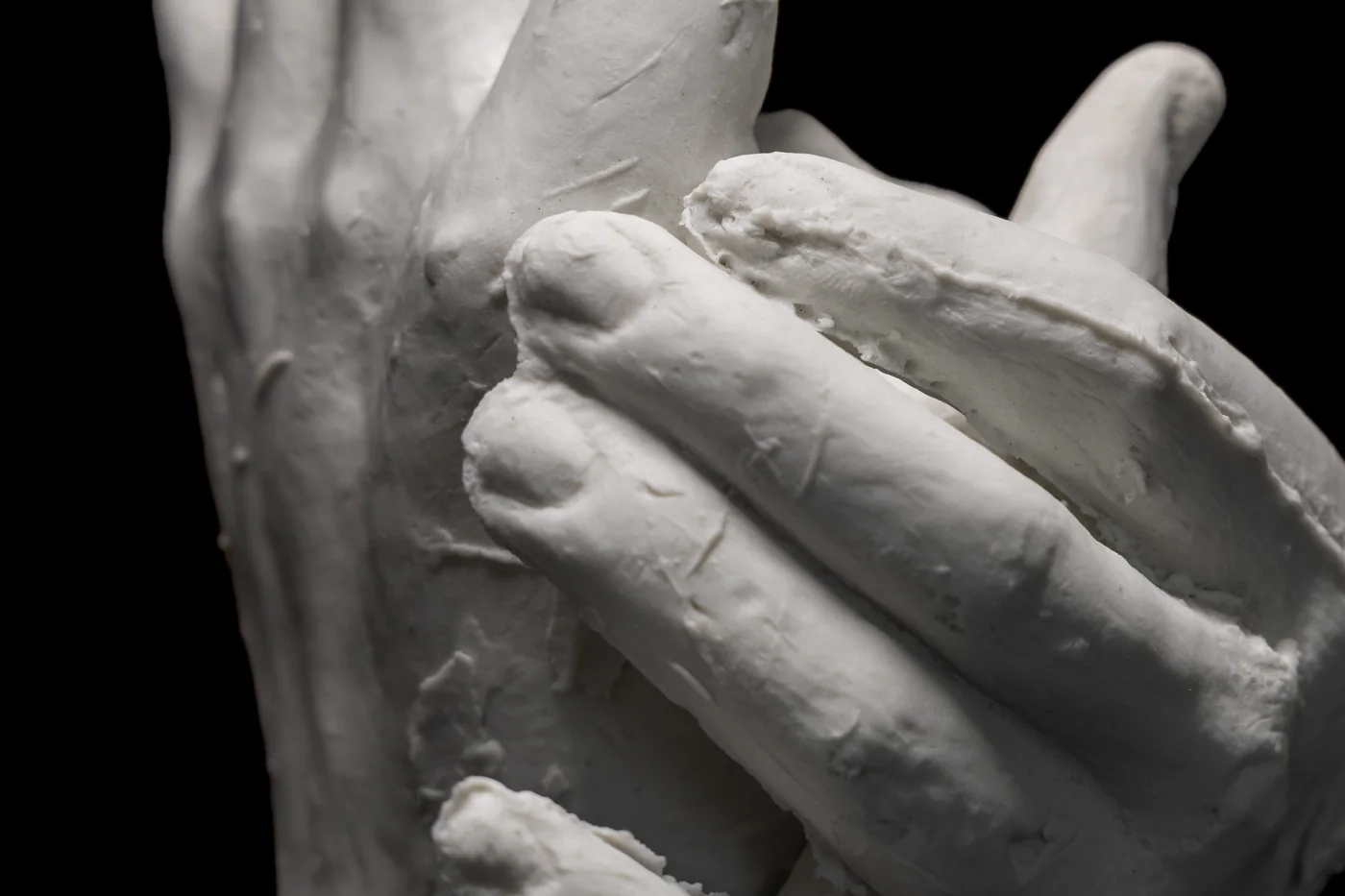 white clay hands, one held across the other, close view against black