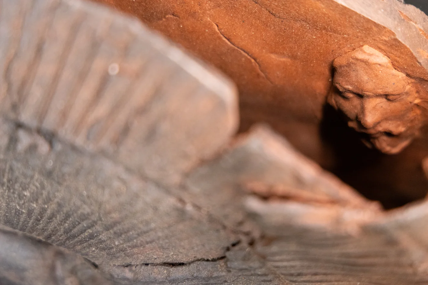 detail of a fan form: a small face in red clay looking out from behind the ribbed edge
